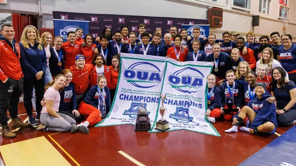 Team group photo in an indoor gym with OUA championship banners and trophies.